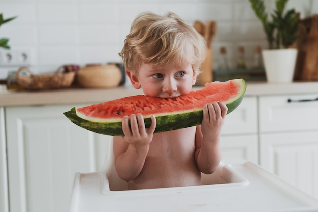 Schattige kleine jongen die sappige watermeloen eet terwijl hij aan de kindertafel zit