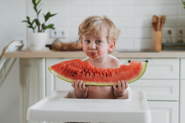 Schattige kleine jongen die sappige watermeloen eet terwijl hij aan de kindertafel zit