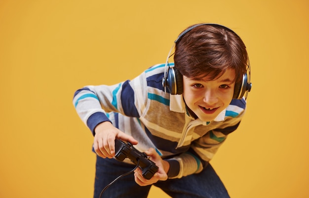 Schattige kleine jongen die videogame speelt in de studio tegen een gele achtergrond.