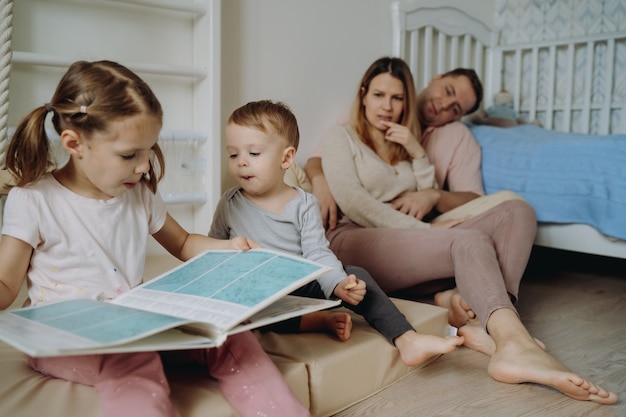 Schattige kleine jongen en een jongen lezen boek in kinderkamer jonge ouders op achtergrond zittend op de vloer...