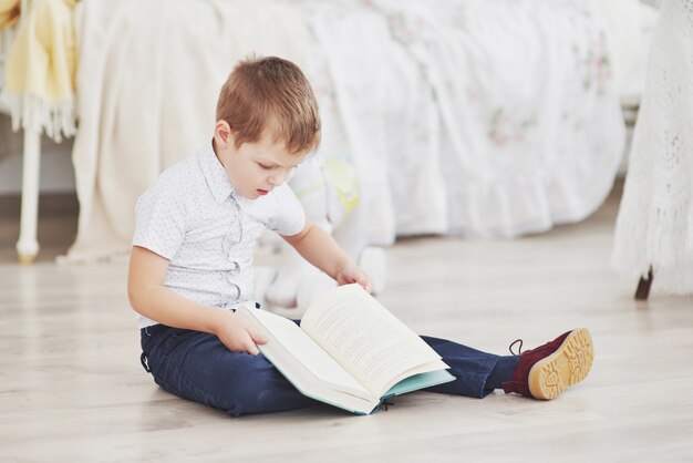 Schattige kleine jongen gaat voor het eerst naar school. Kind met schooltas en boek. Kid maakt een koffer, kinderkamer op een achtergrond. Terug naar school