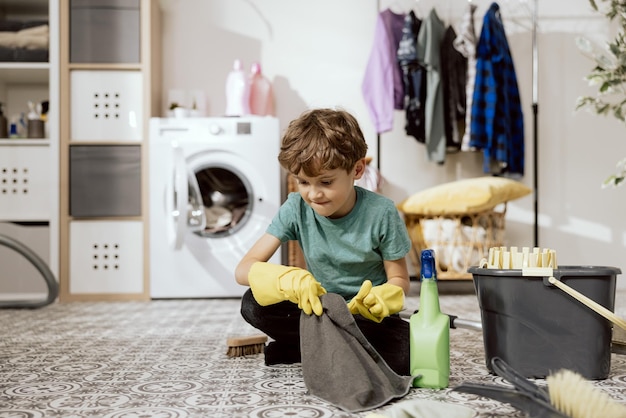 Schattige kleine jongen helpt het huis schoon te maken veegt de vloer af met een doek wast de badkamer