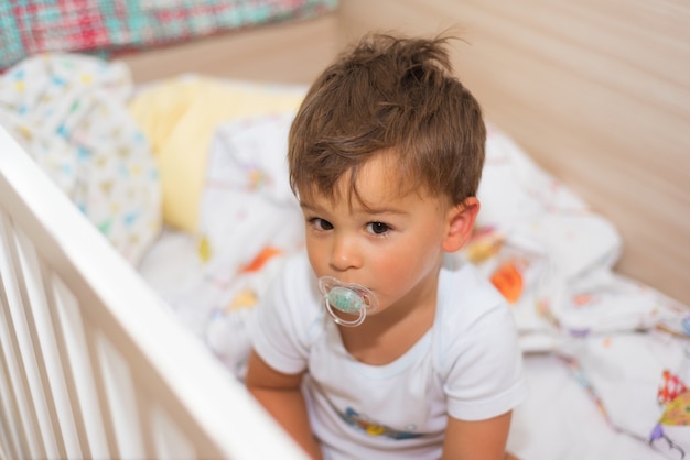 Schattige kleine jongen in de wieg met fopspeen