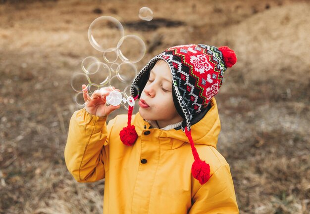 Schattige kleine jongen in een gebreide muts blaast zeepbellen in het herfstpark.