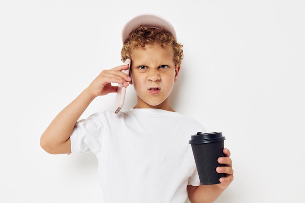 Schattige kleine jongen in een witte t-shirt pet met een telefoon in een glas met een drankje lichte achtergrond ongewijzigd