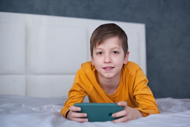 Schattige kleine jongen jongen liggend op het bed gericht op smartphone