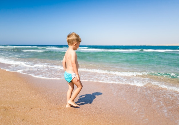 Schattige kleine jongen lopen naar de zee en kijken naar oceaangolven. Kind ontspannen en plezier hebben tijdens de zomervakantie vakantie.