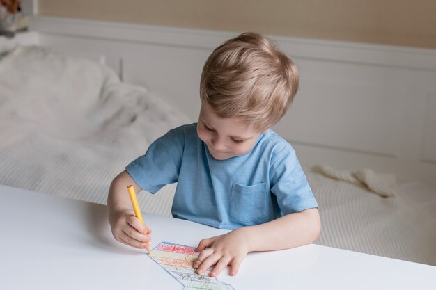 Schattige kleine jongen met blond haar, zittend aan een tafel