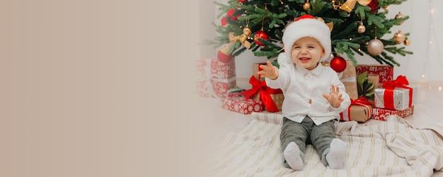 Schattige kleine jongen met een nieuwjaarshoed zit op een deken voor de kerstboom