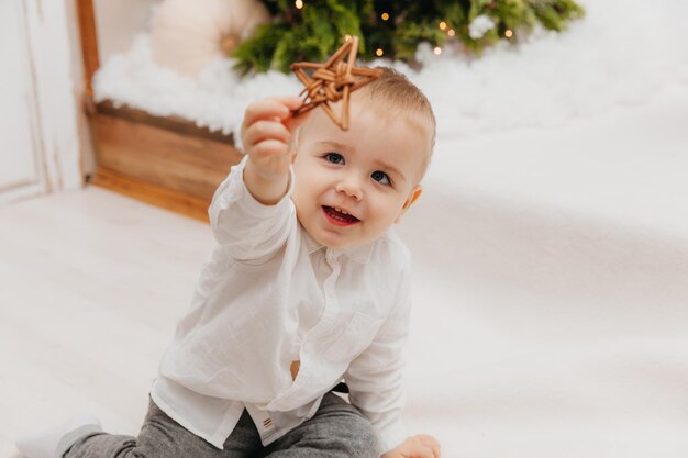 Schattige kleine jongen met een nieuwjaarshoed zit op een deken voor de kerstboom.