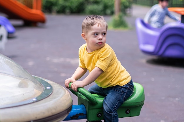 Schattige kleine jongen met het syndroom van Down draaien op Merrygoround carrousel op speelplaats