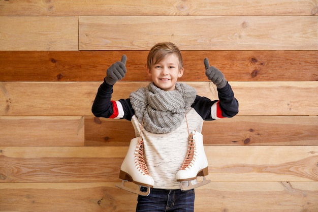 Schattige kleine jongen met ijs-of rolschaatsen duim-omhoog tegen houten tonen