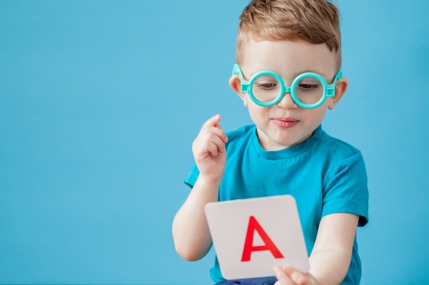 Schattige kleine jongen met letter op blauw. Het kind leert letters.