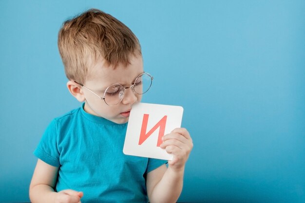 Schattige kleine jongen met letter op blauwe muur. Kind leert brieven. Alfabet