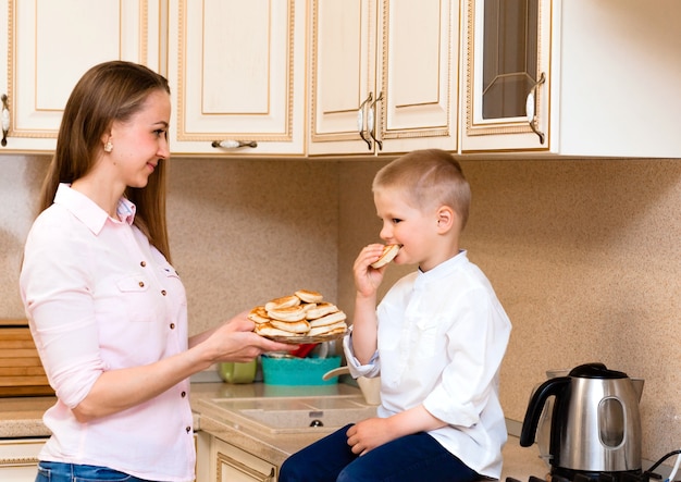 Schattige kleine jongen met moeder. Familie in de keuken. Moeder met zoon die pannenkoeken eet. zelfgemaakt bakken