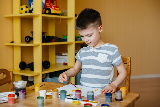 schattige kleine jongen speelt en schildert in zijn kamer.