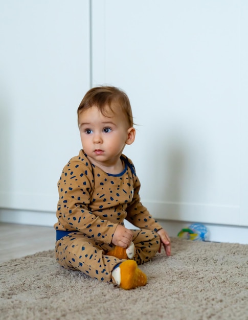 Schattige kleine jongen speelt met speelgoed terwijl hij op de vloer zit Nieuwsgierige babyjongen die kinderkamer bestudeert