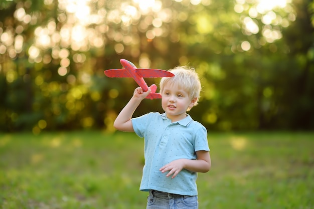 Schattige kleine jongen spelen met speelgoed vliegtuig in het zonnige park.