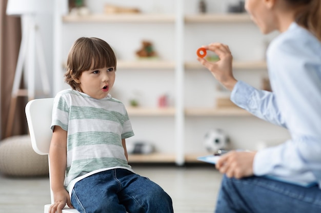 Schattige kleine jongen studeren met professionele vrouw logopedist die geluid o uitspreekt in de klas