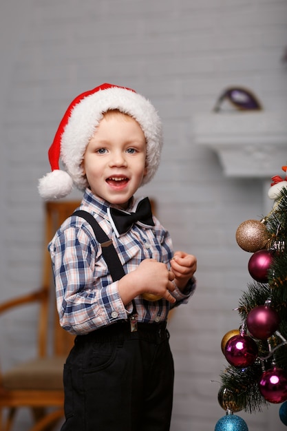 Schattige kleine jongen versiert een kerstboom in het interieur met kerstversiering