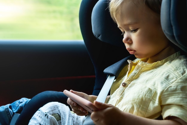 Schattige kleine jongen zit in een babyzitje in een auto