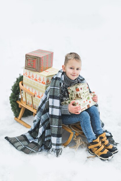 Schattige kleine jongen, zittend op een houten slee versierd met dozen presenteert