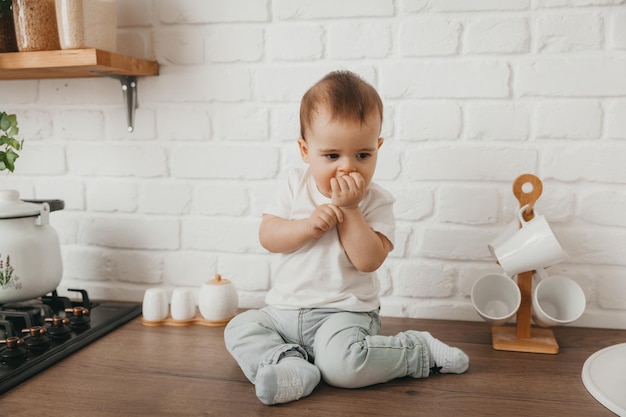 Schattige kleine jongen zittend op het aanrecht in een stijlvolle keuken met zijn blote voeten bungelend