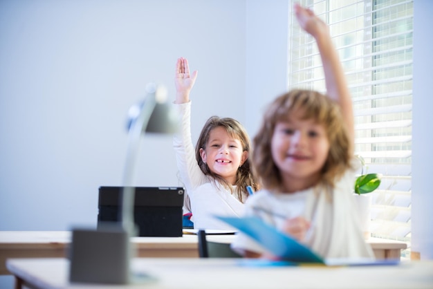 Schattige kleine leerlingen die handen opsteken tijdens les kinderen in de klas op school