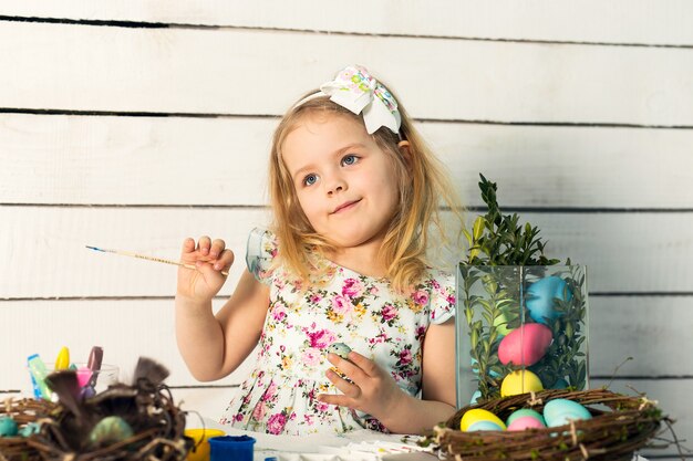 Schattige kleine meisje blonde schildert paaseieren met een penseel in verschillende kleuren. Pasen-thema.