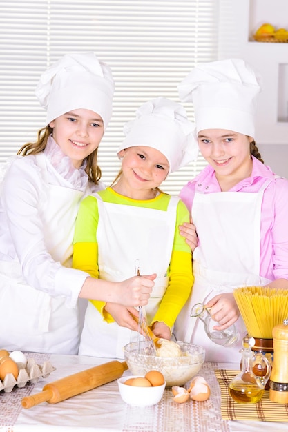 Schattige kleine meisjes in koksmutsen en schorten die deeg bereiden in de keuken