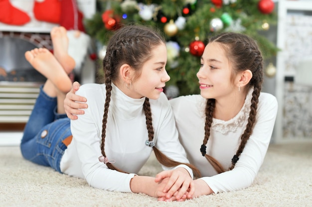 Schattige kleine meisjes liggen in de buurt van versierde kerstboom