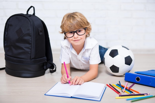 Schattige kleine schooljongen in glazen huiswerk liggend op de vloer