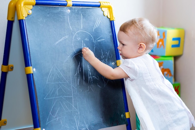 Schattige kleine vrouwelijke kunstenaar schildert op een ezel met krijt terwijl ze op een stoel staat