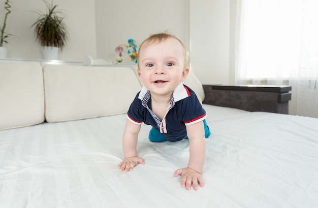 Schattige lachende baby die op bed kruipt en naar de camera kijkt