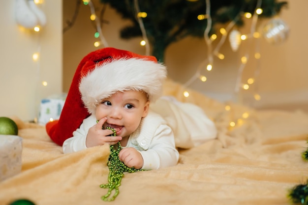 Schattige lachende baby ligt onder een feestelijke kerstboom en speelt met geschenken. Kerst- en nieuwjaarsvieringen.