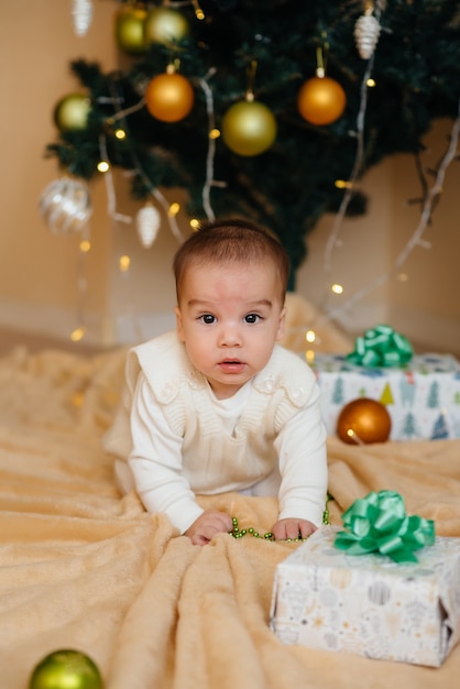 Schattige lachende baby ligt onder een feestelijke kerstboom en speelt met geschenken