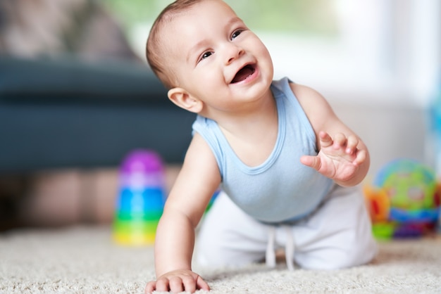 schattige lachende babyjongen die op de vloer in de woonkamer kruipt