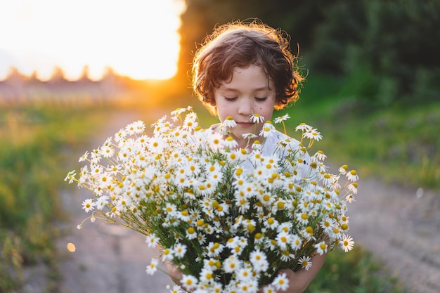 Schattige lachende jongen op kamille veld bij zonsondergang in zacht zonlicht Leven zonder allergieën ademen vrij Jongen en madeliefjes Kind dromen en glimlachen tegen de achtergrond van een kamille veld