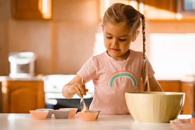 Schattige lachende kleine blonde meisje koken deeg in de keuken thuis