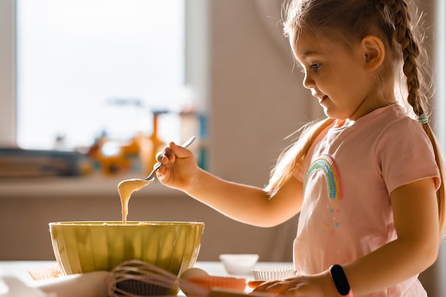 Schattige lachende kleine blonde meisje koken deeg in de keuken thuis