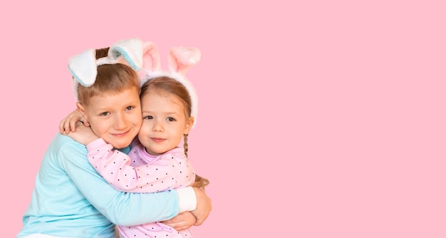 Schattige lachende kleine jongen en meisje met paashaas oren knuffelen kinderen geïsoleerd op roze achtergrond