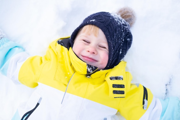 Schattige lachende kleine jongen liggend in een sneeuwjacht, plezier hebben, buiten lachen in het winterbos