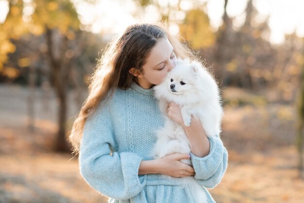 Schattige lachende tienermeisje 15-16 jaar oud houden witte pluizige spitz puppy hond samen in de herfst