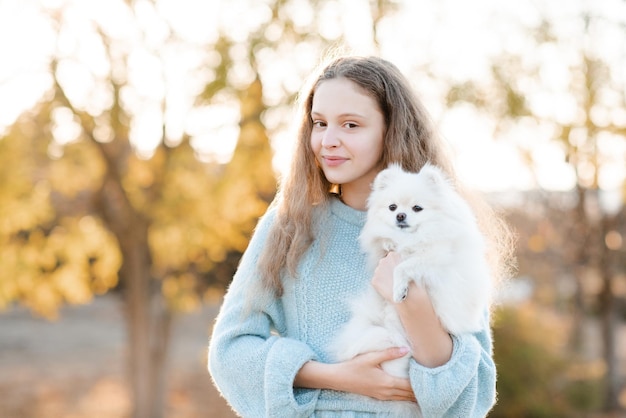 Schattige lachende tienermeisje 15-16 jaar oud houden witte pluizige spitz puppy hond samen in de herfst