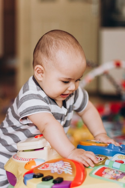 Schattige mollige baby staat en speelt met een muziektafel voor kinderen. Veel kleurrijk speelgoed overal.