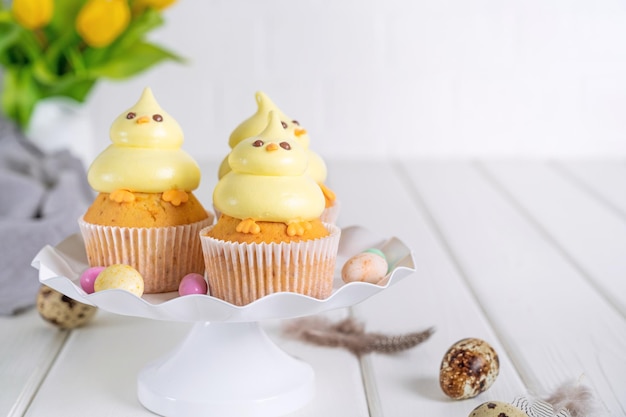 Schattige paaskuiken cupcakes Vanille cupcakes met botercrème op een witte standaard met verse bloemen