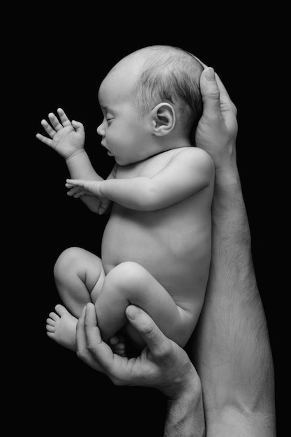 Schattige pasgeboren baby in de handen van de vader op zwarte muur