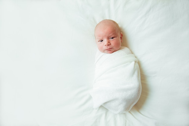 Schattige pasgeboren baby ligt ingebakerd in een witte deken. Kopieer ruimte en bovenaanzicht