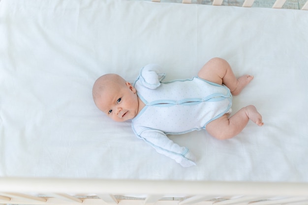 Schattige pasgeboren babyjongen liggend op de achterkant van de wieg op het katoenen bed thuis voordat hij naar bed gaat, babyweek, het concept van geboorte en kinderschoenen, bovenaanzicht.