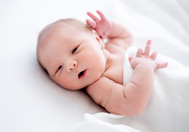 Schattige pasgeboren babymeisje liggend in het bed en in slaap vallen met haar handen dicht bij het hoofd. Lief kind dat thuis rust